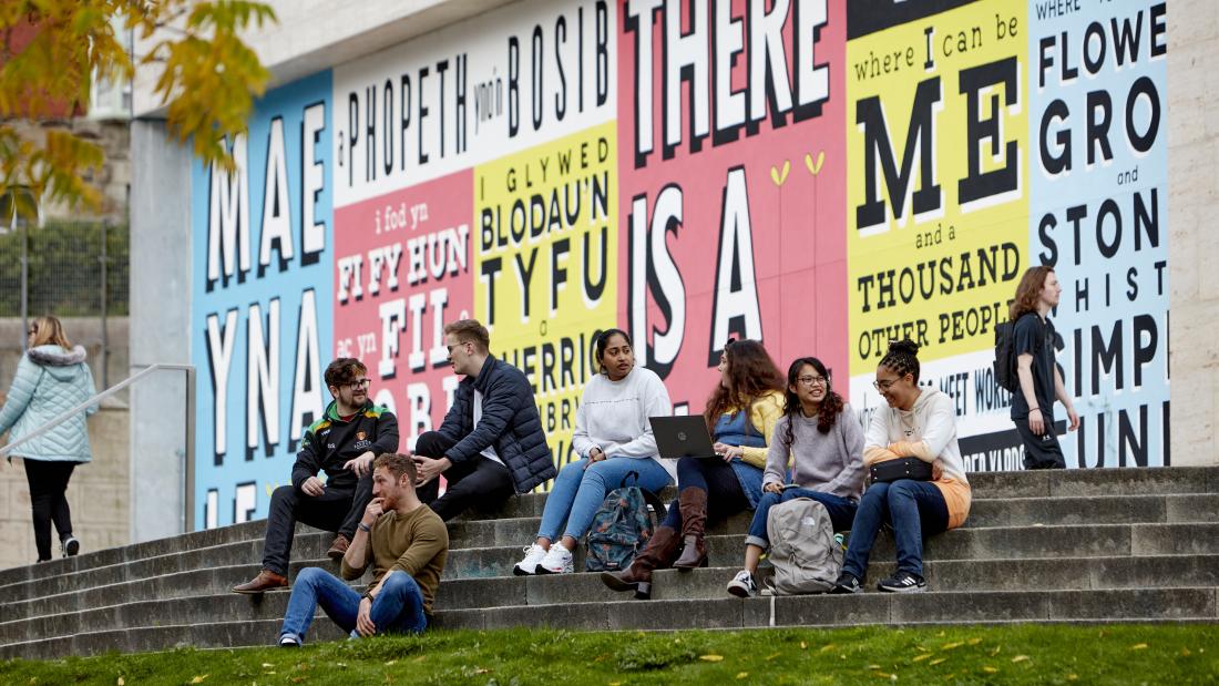 Bangor University students sitting on a stairs with graffiti in the background