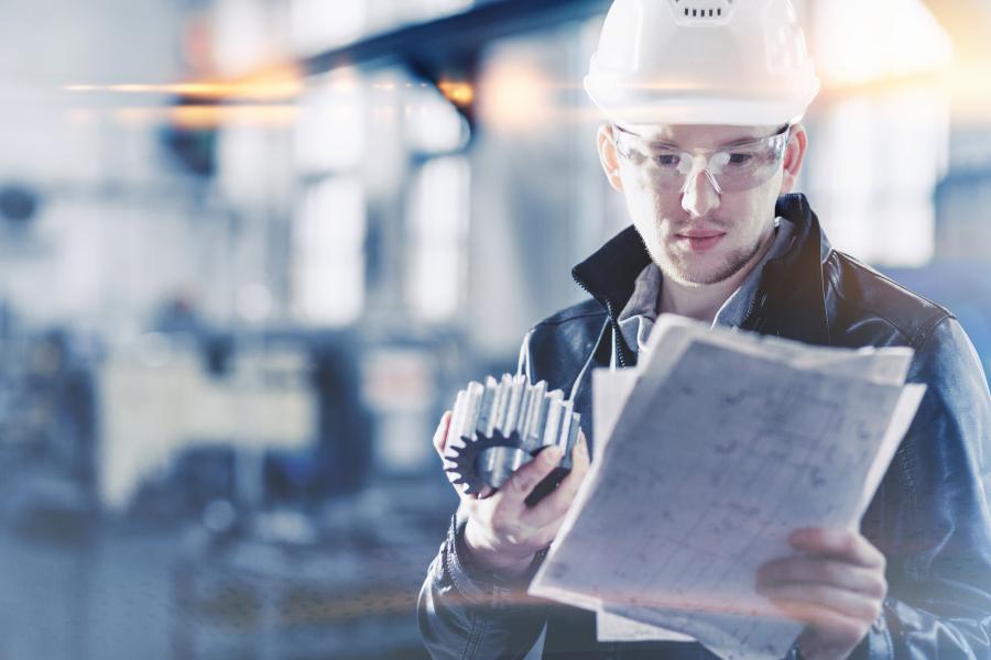 Engineer holding a engineering part and checking paper plans