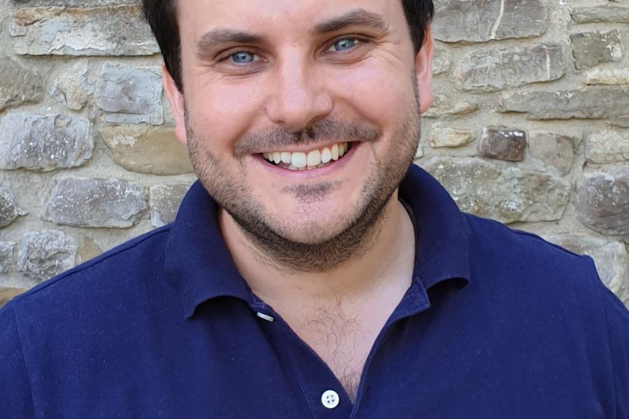 Spiky dark haired man smiles into camera wearing blue shirt