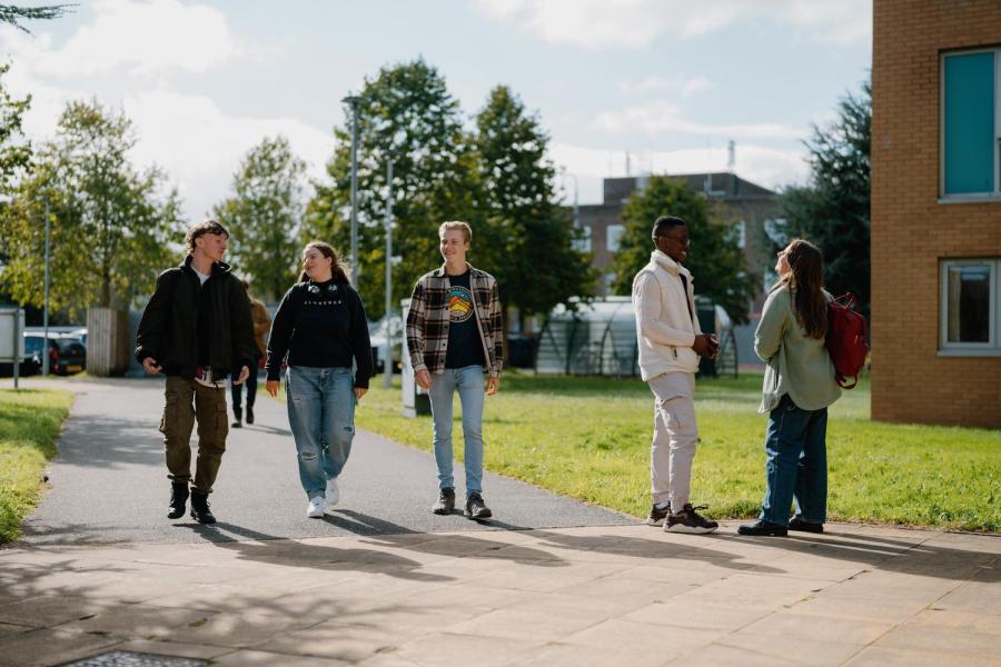 A group of three students are walking towards the camera on the Ffriddoedd site and two other students are chatting
